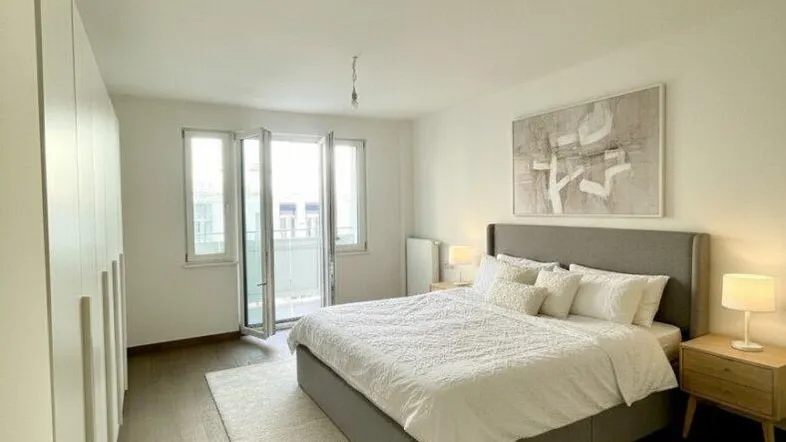 Helles Schlafzimmer mit modernem Bett, Einbauschränken und Zugang zu einem Balkon.