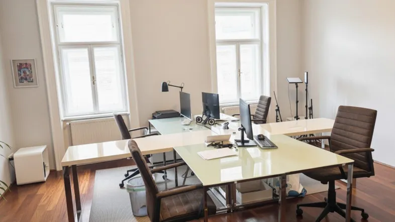 Helles Büro mit mehreren Arbeitsplätzen, großen Fenstern und elegantem Holzboden.