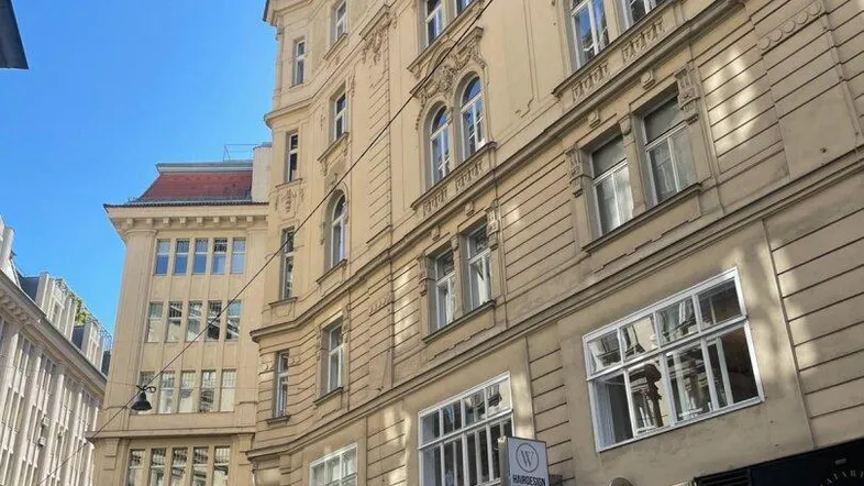 Historische Fassade eines Wiener Gebäudes mit reich verzierten Fenstern und Geschäften im Erdgeschoss unter blauem Himmel.