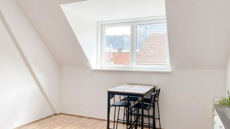 Helles Dachgeschosszimmer mit Holzboden, Schrägfenster und kleinem Esstisch.