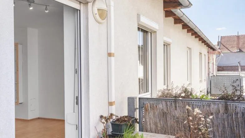 Heller Balkon mit Fliesenboden, Pflanzen und Zugang zu einem Innenraum mit Parkett.