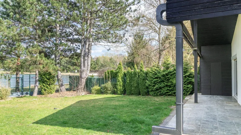 Gepflegter Gartenbereich mit Rasenfläche, hohen Bäumen und einer überdachten Terrasse am Haus.