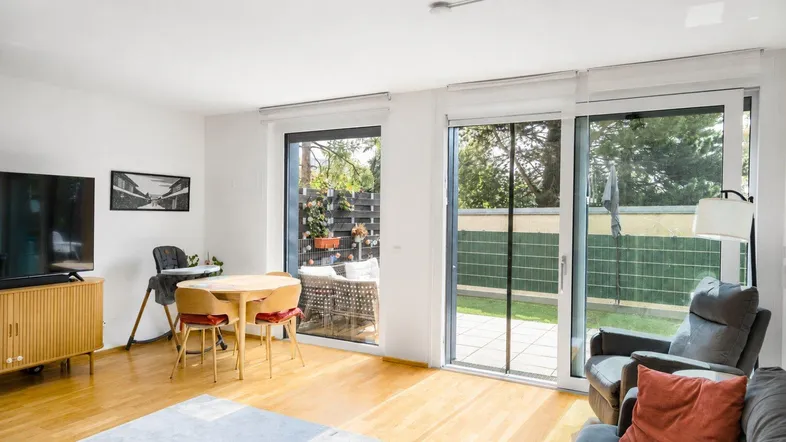 Helles Wohnzimmer mit Holzboden, Zugang zur Terrasse und kleinem Essbereich.