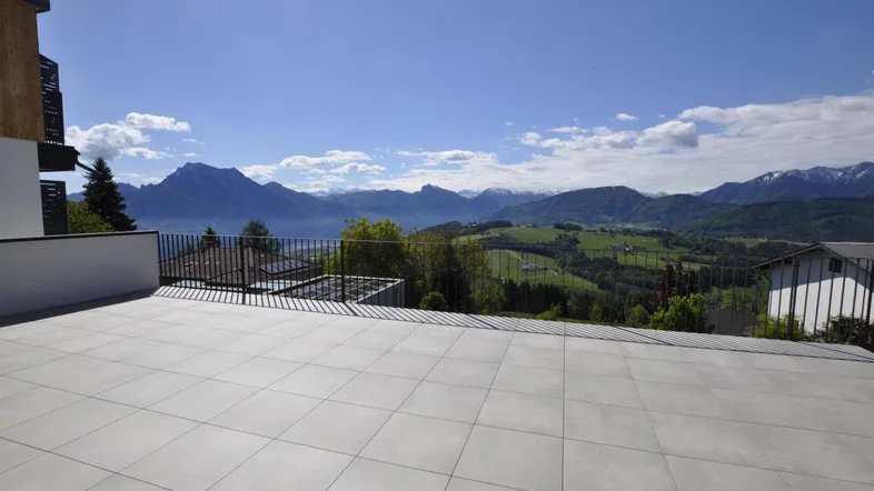 Große geflieste Terrasse mit weitem Blick auf die umliegende Berglandschaft und den See.