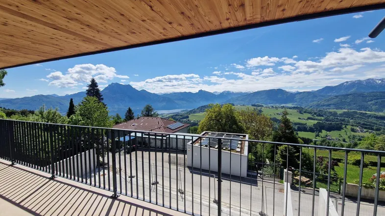 Geräumiger Balkon mit Holzdach und atemberaubendem Blick auf die Berge und den See.