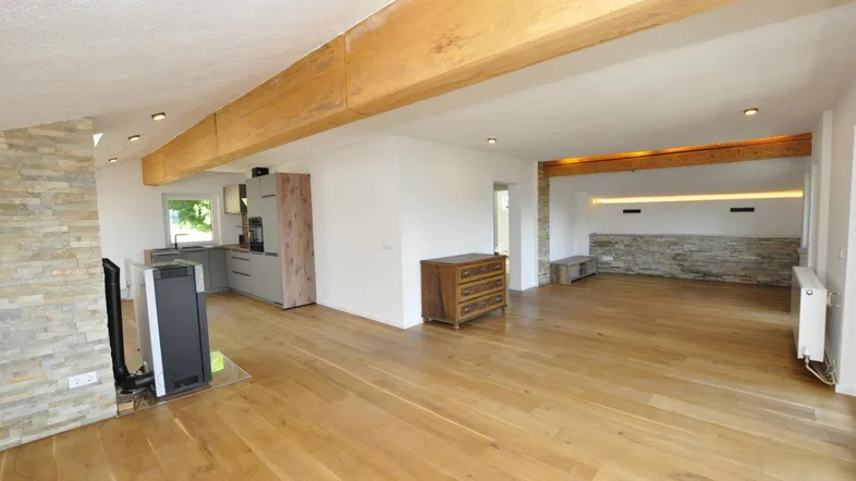 Offener Wohn- und Essbereich mit Holzboden, Holzbalken und integrierter moderner Küche.