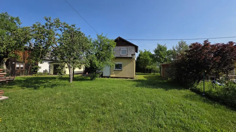 Gepflegter Gartenbereich mit Rasenfläche, Obstbäumen und einem kleinen Haus im Hintergrund unter blauem Himmel.