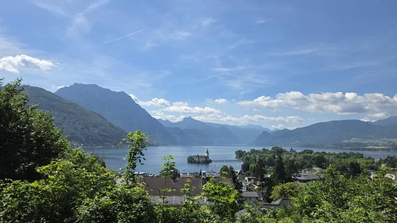 Panoramablick auf einen großen See, umgeben von Bergen, mit einer Stadt und einer Inselburg im Vordergrund.