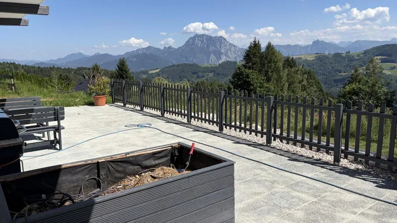 Geräumige Terrasse mit Bergblick, umgeben von einer Holzumzäunung und grüner Landschaft.