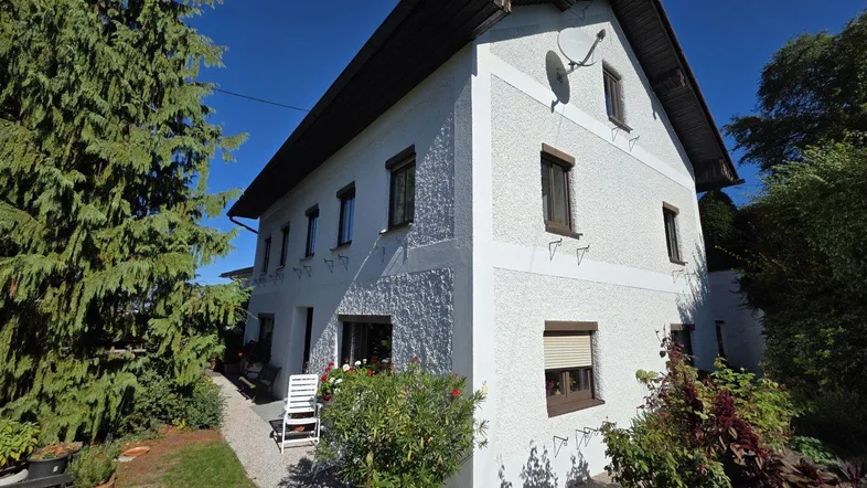 Charmantes Einfamilienhaus mit weißer Fassade, braunen Fensterläden und einem kleinen, sonnigen Terrassenbereich.