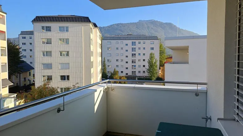 Heller Balkon mit Blick auf umliegende Gebäude und die Berge im Hintergrund.