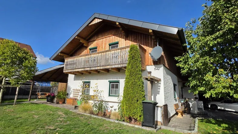 Traditionelles Haus mit Holzfassade, Balkon und gepflegtem Garten unter blauem Himmel.