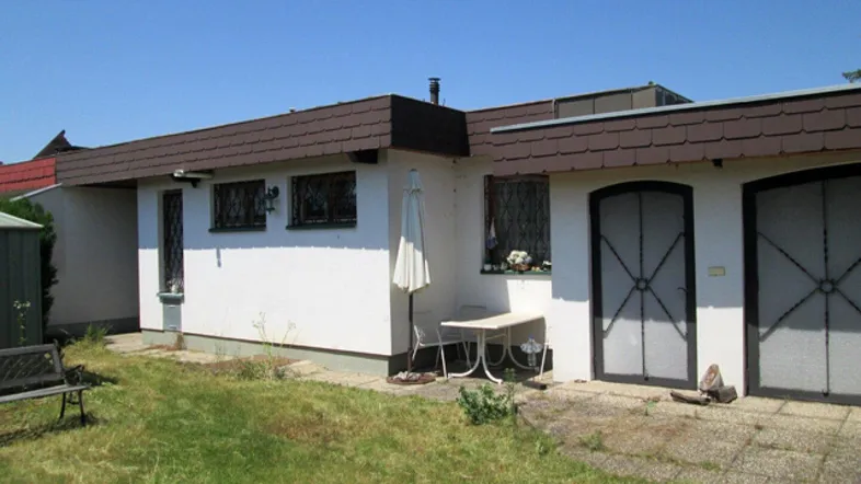 Seitenansicht des Hauses mit Rasenfläche und einem kleinen gepflasterten Bereich im Freien.