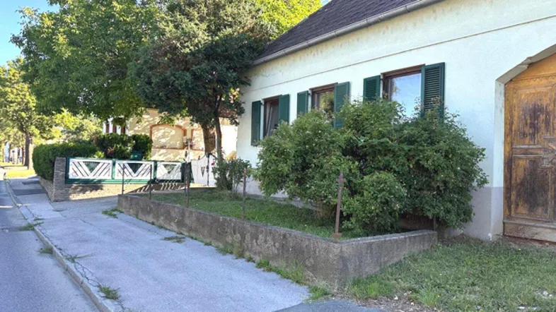 Seitenansicht eines traditionellen Hauses mit grünen Fensterläden und einem kleinen Vorgarten.