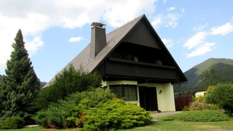 Traditionelles Haus mit Satteldach, umgeben von viel Grün und Bäumen.