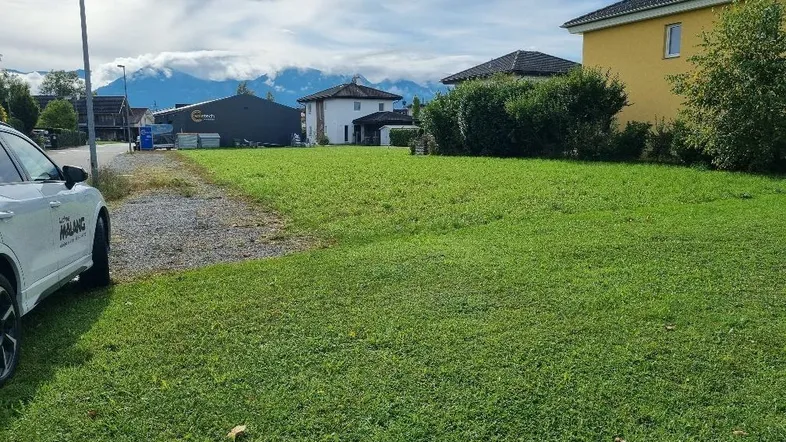 Grüne Wiese mit Blick auf umliegende Häuser und die majestätische Berglandschaft unter bewölktem Himmel.