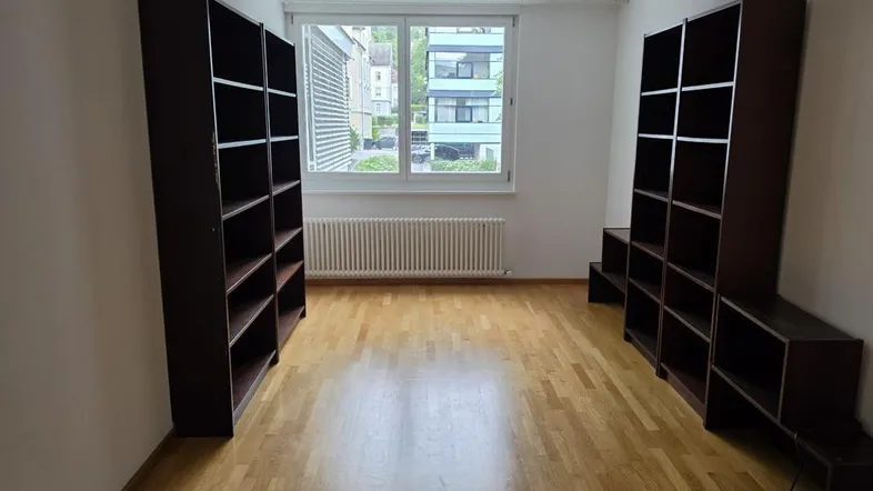 Helles Zimmer mit Parkettboden, weißen Wänden und zwei Bücherregalen, ideal als Wohn- oder Arbeitsbereich.