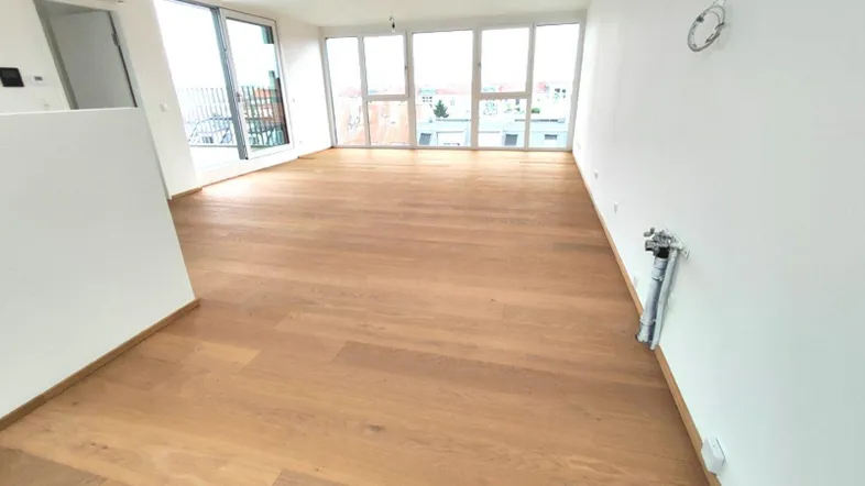 Heller, leerer Wohnbereich mit großen Fenstern und Holzboden, bereit für die Einrichtung.