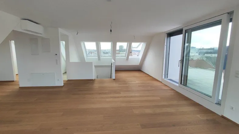Helles und geräumiges Dachgeschosszimmer mit Holzboden und großen Fenstern, die viel Tageslicht hereinlassen.