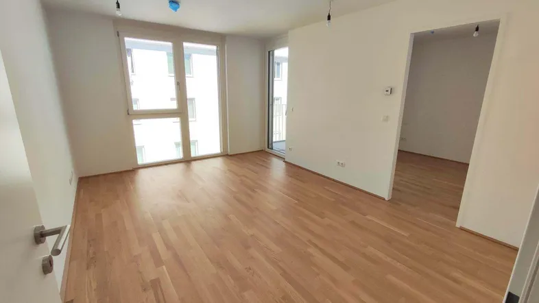 Heller Wohnbereich mit Parkettboden und Zugang zum Balkon, bereit für die Einrichtung.