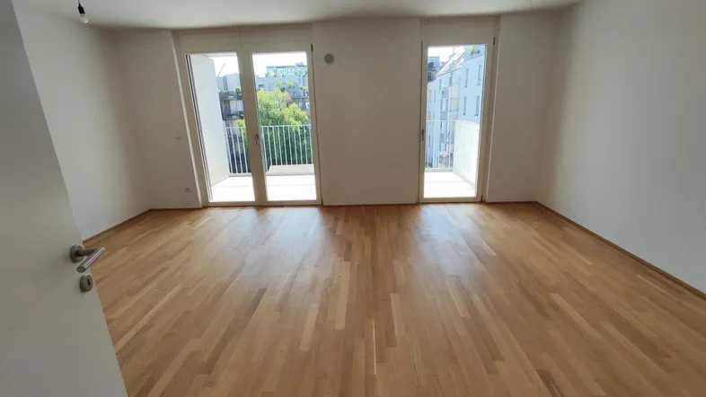 Helles, leeres Zimmer mit Parkettboden und zwei Balkonzugängen, ideal für viel Tageslicht.