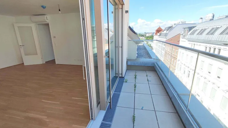 Heller Innenraum mit Holzboden und großem Schiebefenster, das zu einem Balkon mit Stadtblick führt.