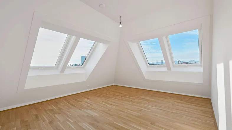 Helles Dachzimmer mit schrägen Wänden, Holzboden und zwei großen Dachfenstern für viel Tageslicht.