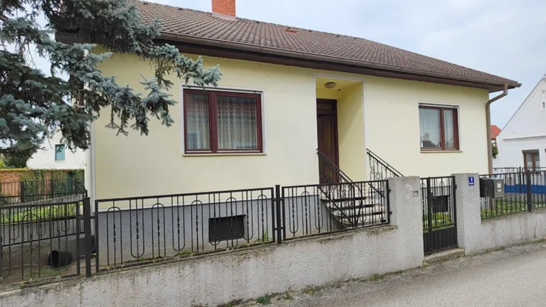 Einfamilienhaus mit gelber Fassade und braunem Dach in ländlicher Umgebung.