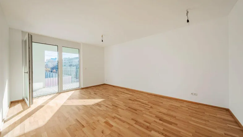 Helles, leeres Wohnzimmer mit Parkettboden und Zugang zu einem Balkon, ideal für individuelle Gestaltung.