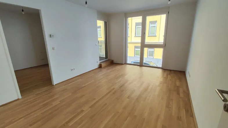 Helles Zimmer mit Parkettboden und Zugang zu einem kleinen Balkon, Blick auf die Straße.
