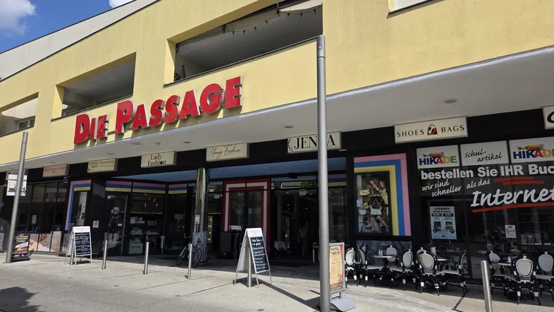 Fassade eines modernen Geschäftsgebäudes mit dem Schriftzug "Die Passage" und mehreren Ladenfronten.