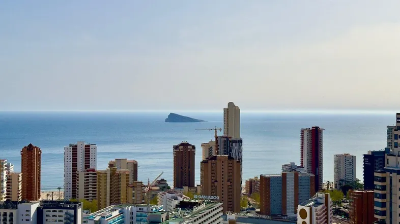 Panoramablick auf die Stadt Benidorm mit Hochhäusern und dem Mittelmeer im Hintergrund.