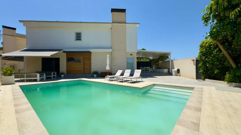 Moderne Villa mit großem Swimmingpool und sonnigem Außenbereich unter blauem Himmel.