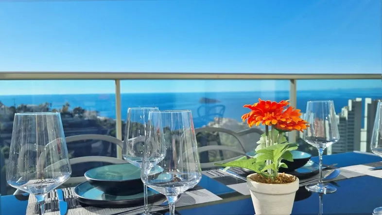 Nahaufnahme eines gedeckten Tisches auf dem Balkon mit Weingläsern und einem weiten Meerblick.