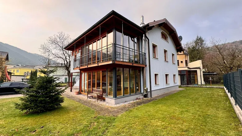 Hausfassade mit großzügigen Glasflächen, Balkon und gepflegtem Rasenbereich.