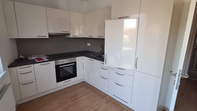 Moderne Einbauküche mit weißen Hochglanzfronten, dunkler Arbeitsplatte und Holzfußboden.