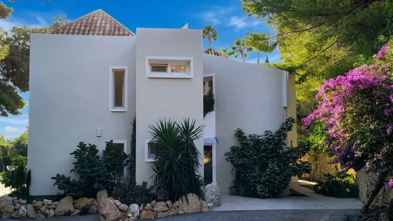 Moderne Villa mit heller Fassade, umgeben von mediterraner Vegetation und blühenden Pflanzen.
