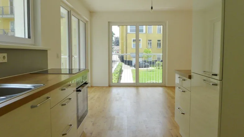 Helle Küche mit Holzarbeitsplatte, Parkettboden und Zugang zum Balkon mit Blick ins Grüne.