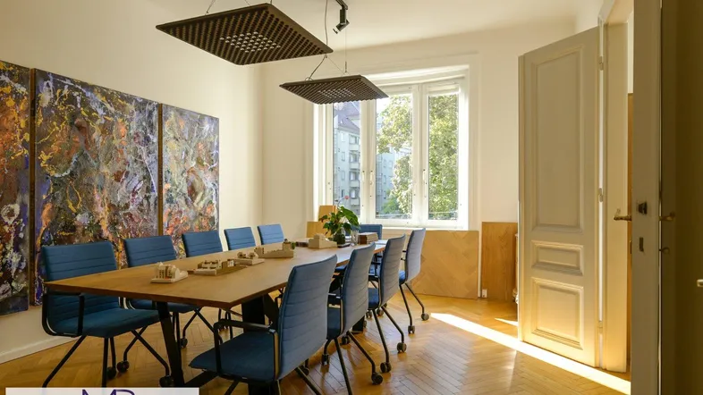 Helles Büro mit großem Konferenztisch, blauen Stühlen und Parkettboden, ideal für Besprechungen.