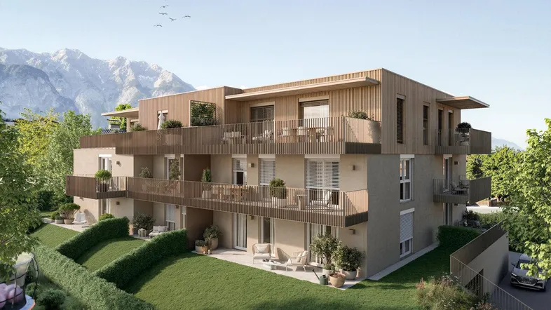 Moderne Wohnanlage mit Holzfassade und Balkonen vor alpiner Bergkulisse.
