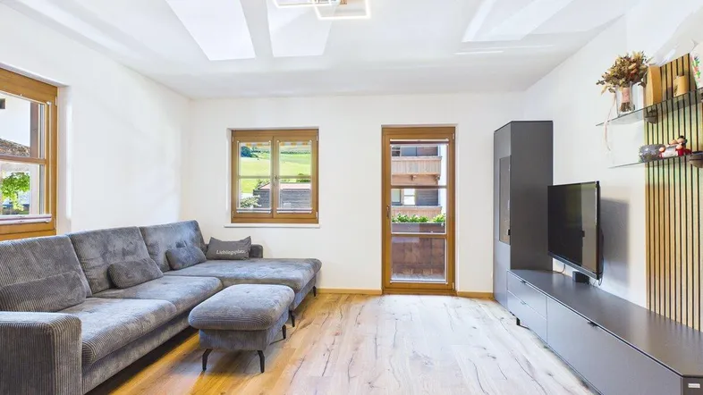 Helles Wohnzimmer mit modernem Sofa, Holzboden und Zugang zum Balkon mit Blick ins Grüne.
