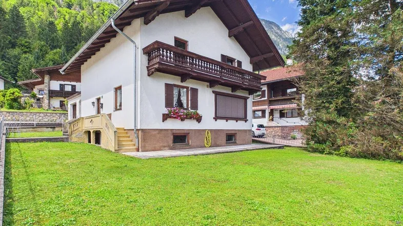 Traditionelles Haus mit weißer Fassade, Holzbalkonen und gepflegtem Garten in alpiner Umgebung.
