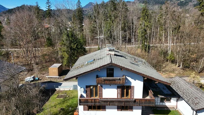 Freistehendes Haus mit Satteldach und Balkonen, umgeben von Bäumen und Bergen.