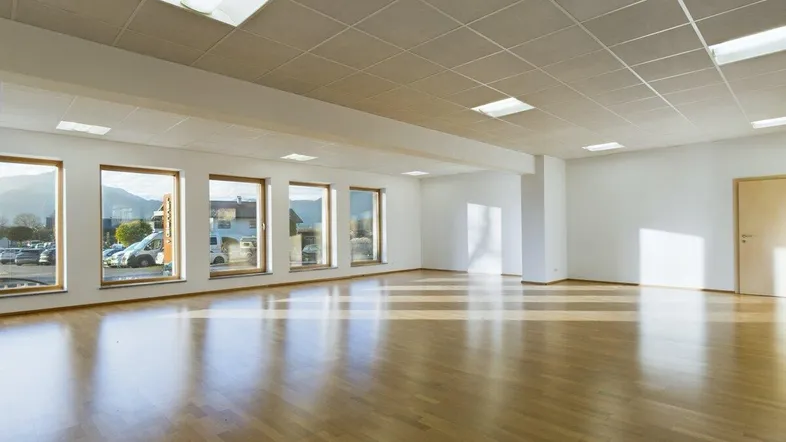 Großer, heller Büroraum mit Holzboden und vielen Fenstern, die viel Tageslicht hereinlassen.
