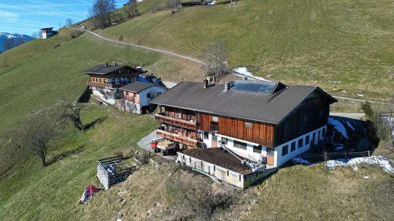 Luftaufnahme eines traditionellen Gebäudes in einer grünen Hanglage mit weiteren Häusern im Hintergrund.