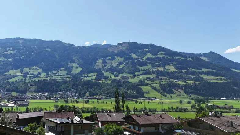 Panoramablick auf das Tal mit grünen Wiesen und majestätischen Bergen im Hintergrund unter blauem Himmel.