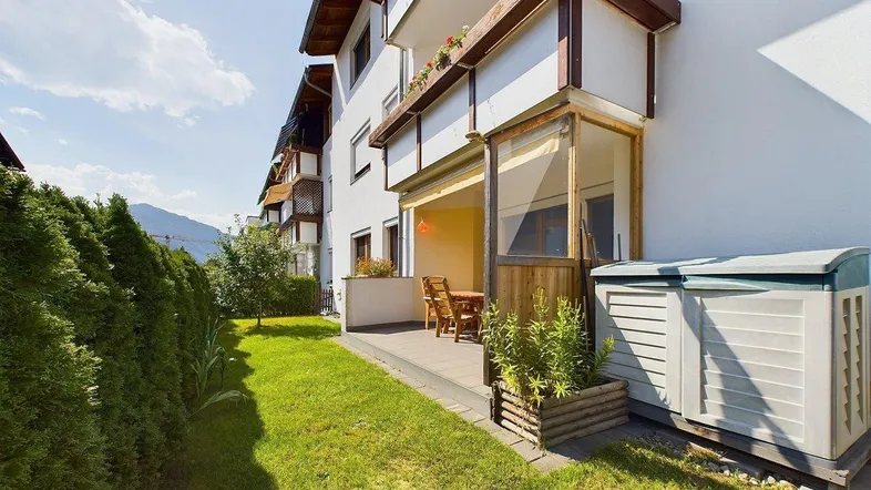 Gepflegte Terrasse mit Gartenmöbeln und angrenzendem Rasenbereich, umgeben von einer hohen Hecke.