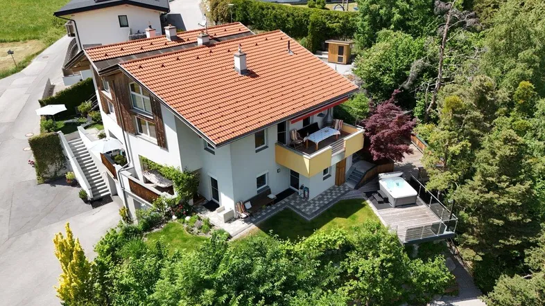 Vogelperspektive eines Hauses mit rotem Ziegeldach, Balkon, Whirlpool und üppiger grüner Umgebung.