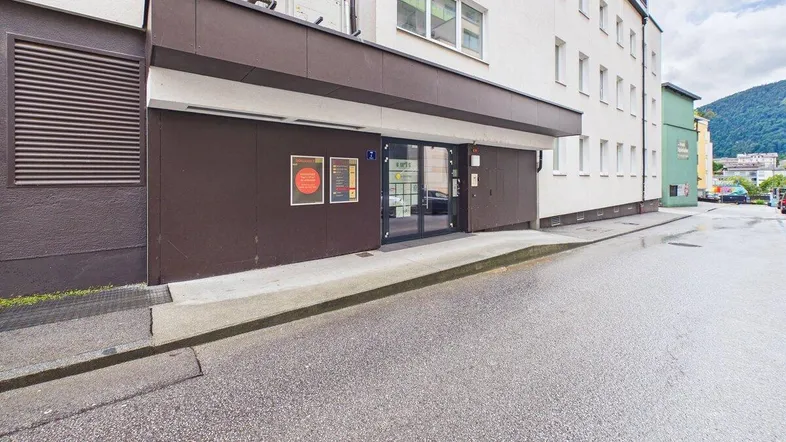 Eingangsbereich eines Geschäftsgebäudes mit brauner Fassadenverkleidung und großen Glastüren von der Straße aus gesehen.