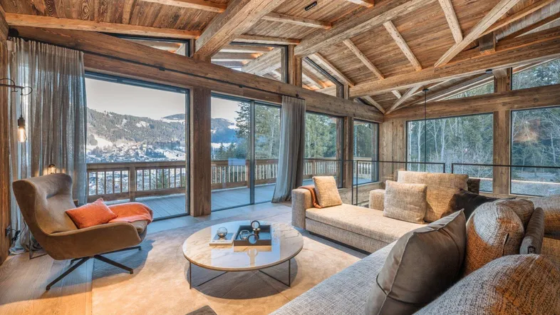 Geräumiges Wohnzimmer im Chalet-Stil mit Holzbalken, großen Fenstern und atemberaubendem Bergblick.